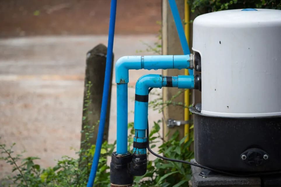 An outdoor commercial water treatment and softener installation system is connected to blue plumbing pipes beside a building in Lake Havasu City, Arizona. The image shows a large water treatment tank with connected PVC water lines and filtration plumbing equipment designed to improve water quality and reduce hard water buildup for residential and commercial properties. Plumbing by Jake provides commercial water treatment and softener installation services in Lake Havasu City AZ including outdoor filtration systems, water softeners, and hard water treatment solutions for Arizona properties.