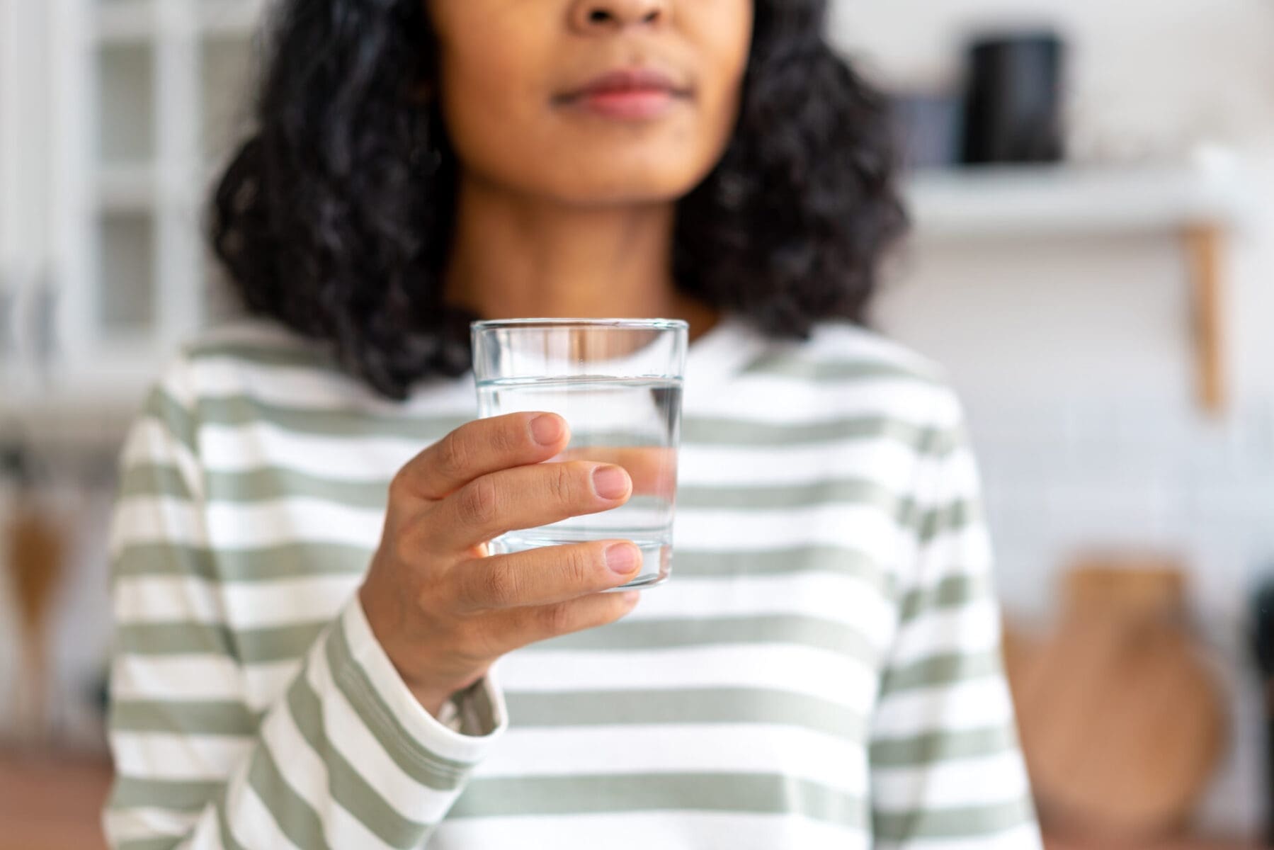 Plumbing by Jake provides commercial water treatment and water softener installation services in Mohave Valley, Arizona to help homeowners and businesses improve water quality and reduce hard-water problems. This image shows a homeowner holding a glass of clean filtered drinking water inside a bright kitchen environment, representing the benefits of professional water filtration and water softener systems. The clean water appearance highlights improved taste, reduced mineral buildup, and healthier water quality commonly achieved with reverse osmosis systems and water treatment equipment in Arizona properties.