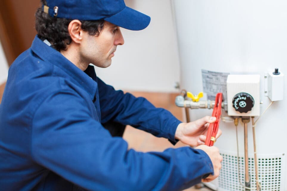 Professional plumber inspecting and servicing a residential hot water system during a Tankless Water Heater Installation in Bullhead City, AZ. The image shows a technician using professional tools while checking water heater controls, plumbing connections, shut-off valves, and system components to ensure safe and reliable operation. Plumbing by Jake provides tankless water heater installation, replacement, repair, and maintenance services in Bullhead City, Arizona.