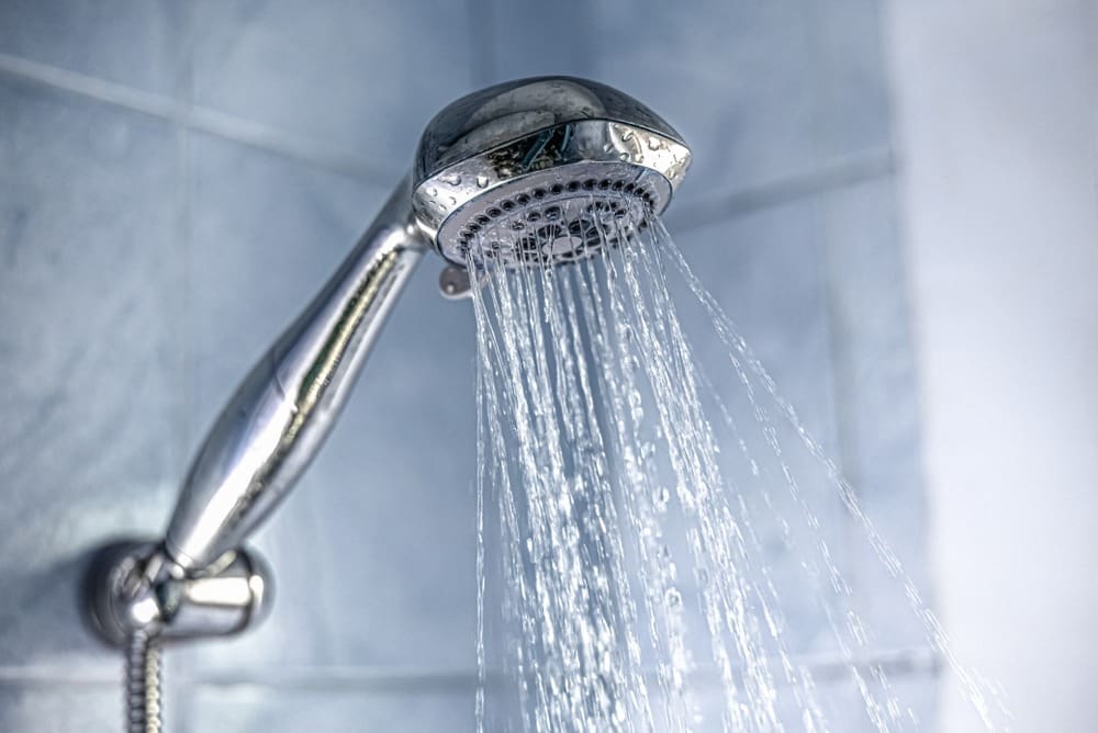 A chrome handheld shower head releases a strong and consistent stream of hot water inside a clean residential bathroom. This image represents Tankless Water Heater Installation in Kingman, AZ by Plumbing by Jake and highlights the reliable hot water performance homeowners expect after a new system installation. The bathroom features modern plumbing fixtures, clean tile surfaces, and clear flowing water that reflects dependable daily comfort.