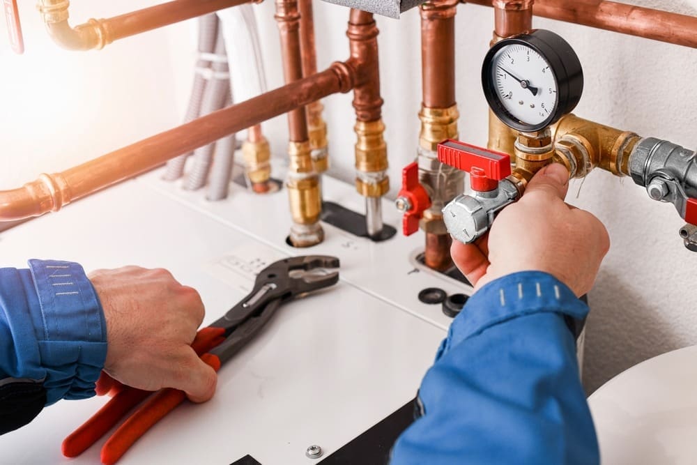 A plumbing technician adjusts valves and plumbing connections during a tankless water heater installation in Mohave Valley, Arizona. The image shows copper water lines, brass fittings, pressure gauges, shut-off valves, and professional plumbing tools used to complete a residential hot water system installation. Plumbing by Jake provides tankless water heater installation services in Mohave Valley, AZ, helping homeowners improve energy efficiency and maintain reliable hot water throughout the year.