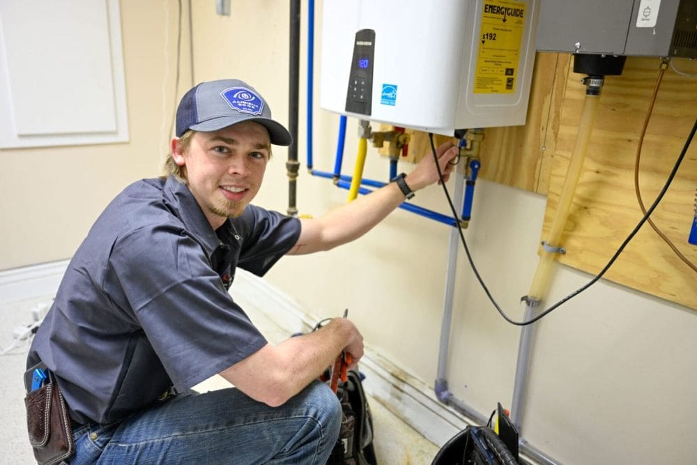 A licensed plumbing technician performs a final inspection during a tankless water heater installation in Mohave Valley, Arizona. The image shows a wall-mounted tankless water heater with visible PEX water lines, plumbing fittings, shut-off valves, and professional installation components inside a residential utility room. Plumbing by Jake provides tankless water heater installation services in Mohave Valley, AZ, helping homeowners improve hot water reliability and reduce energy consumption.